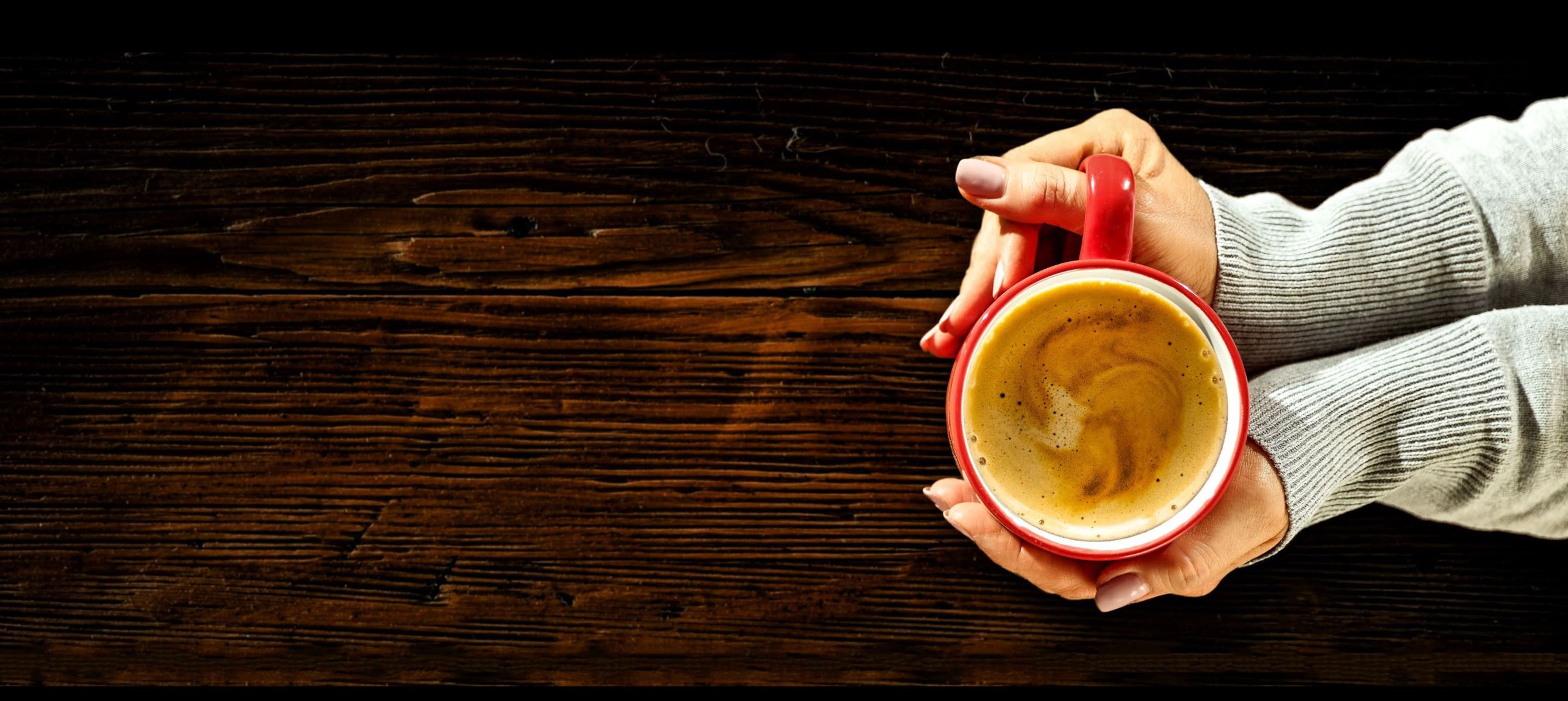 Woman's hands holding a coffee cup on a wooden surface