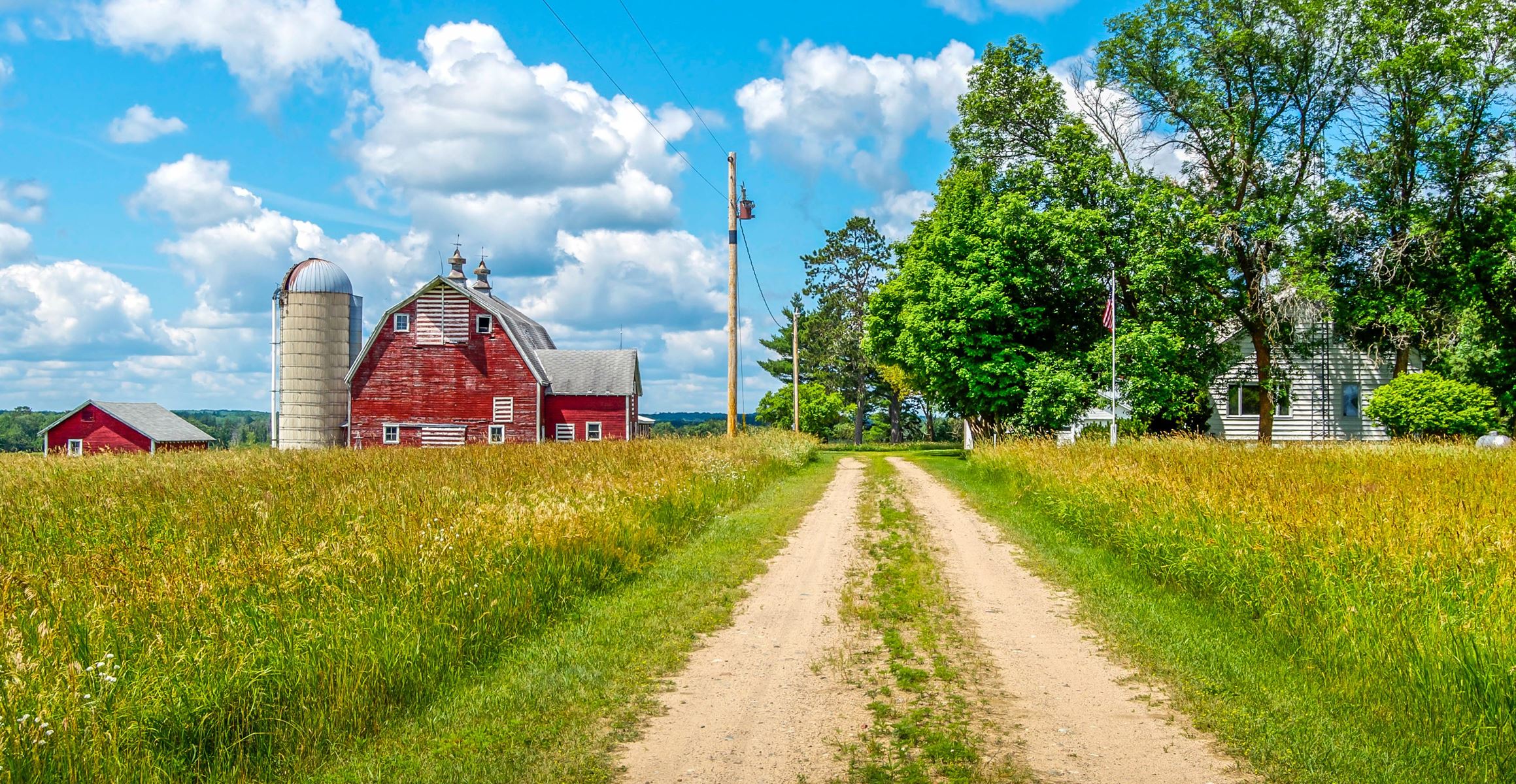 Driveway up to a farm with a red barn and blue sky