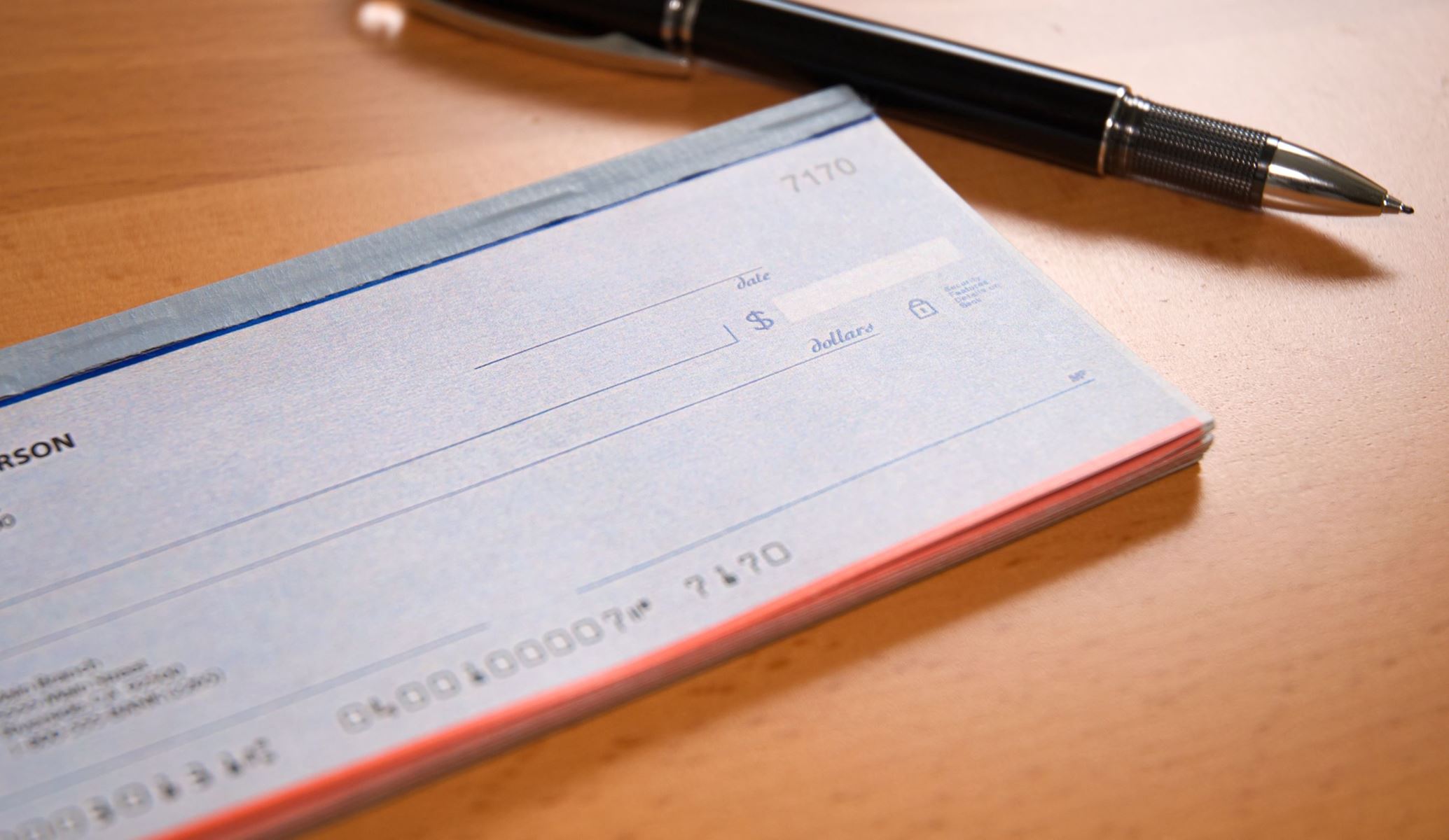 Blank checkbook laying on a table next to a pen