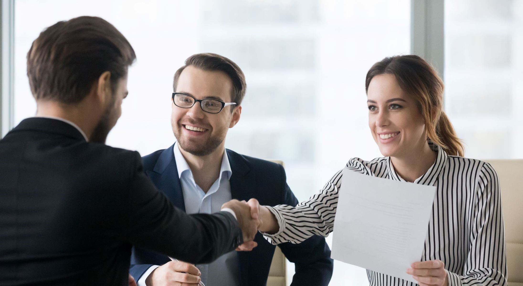 Man and woman smiling and shaking hands with another man.